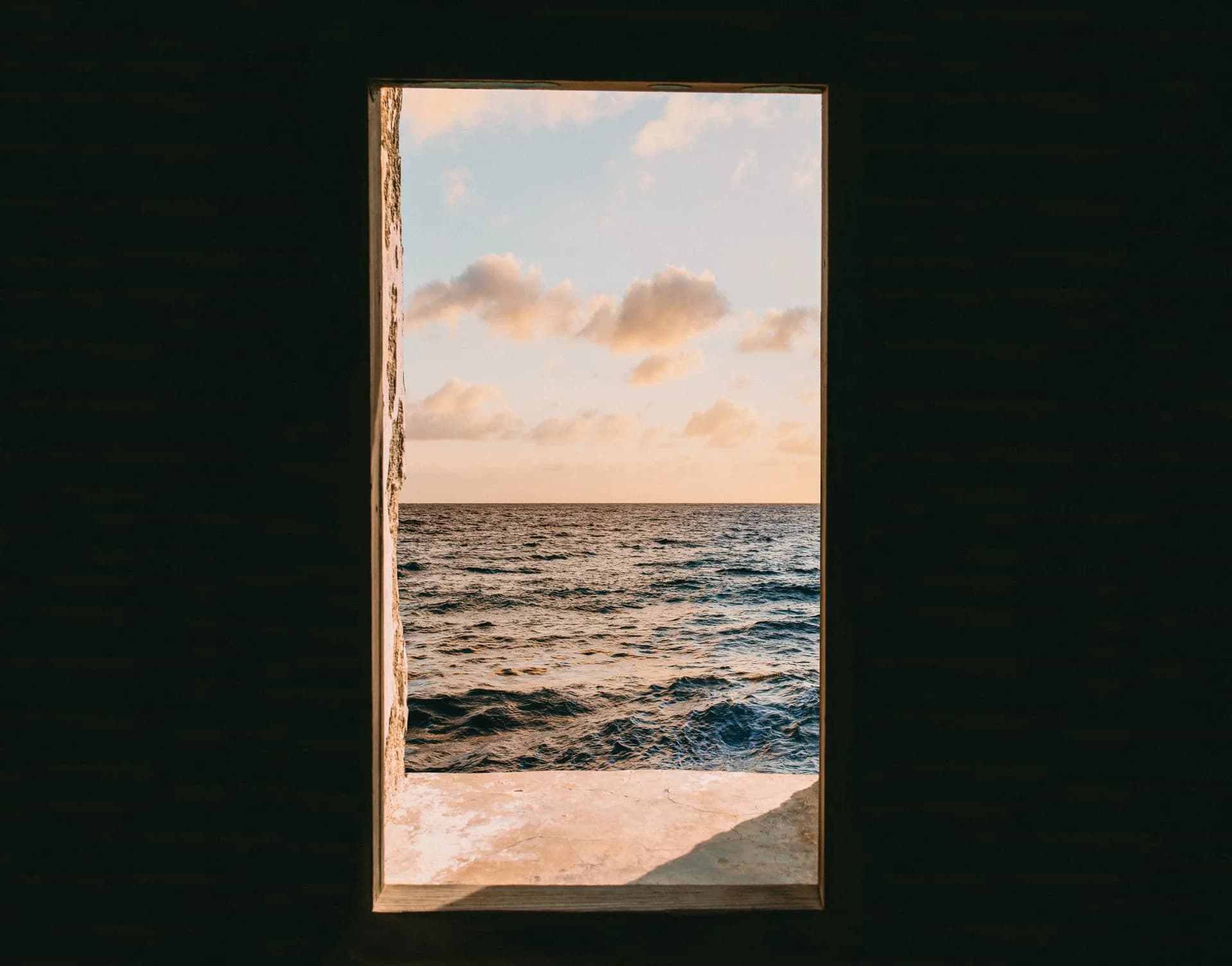 A window overlooking the ocean during golden hour, with warm light reflecting off the water